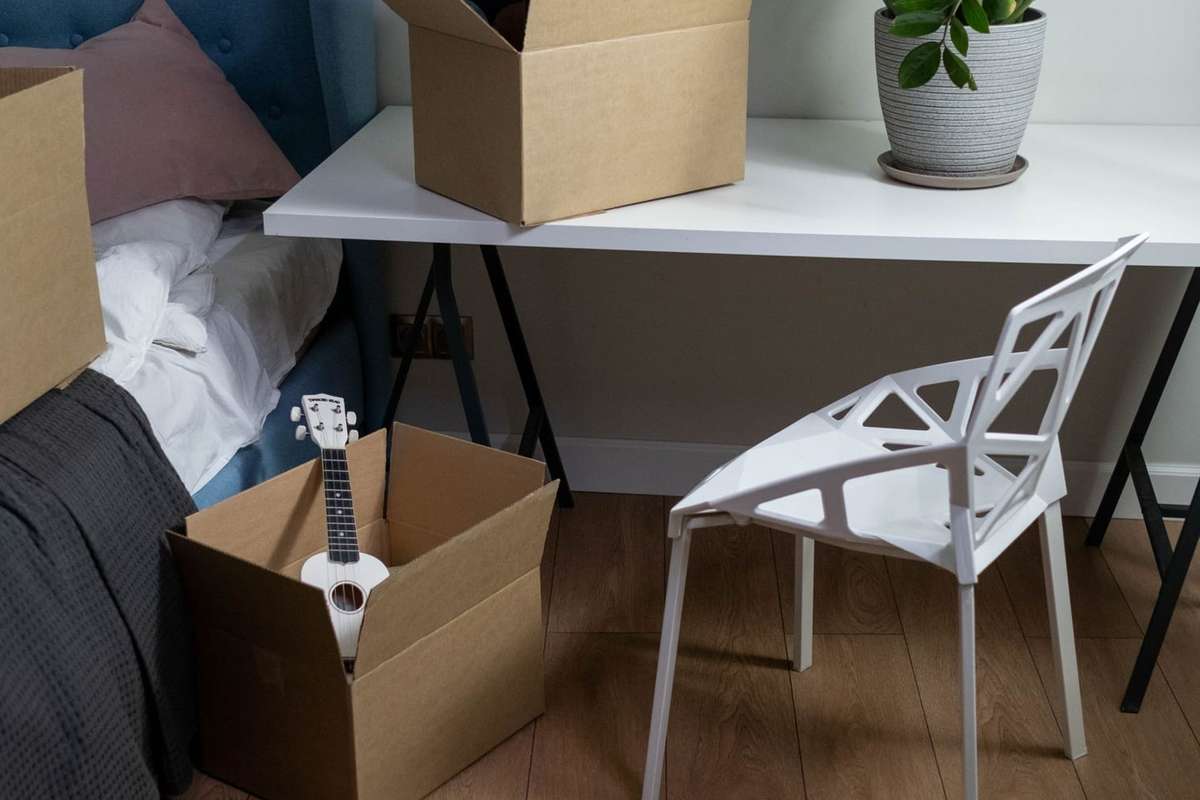 Cajas abiertas junto a una mesa, una silla blanca y una planta