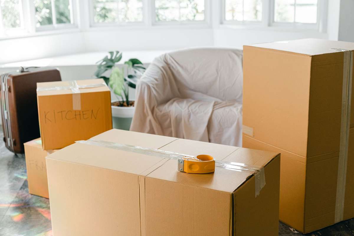 Cajas de cartón precintadas en un salón, junto a un sofá cubierto con una sábana
