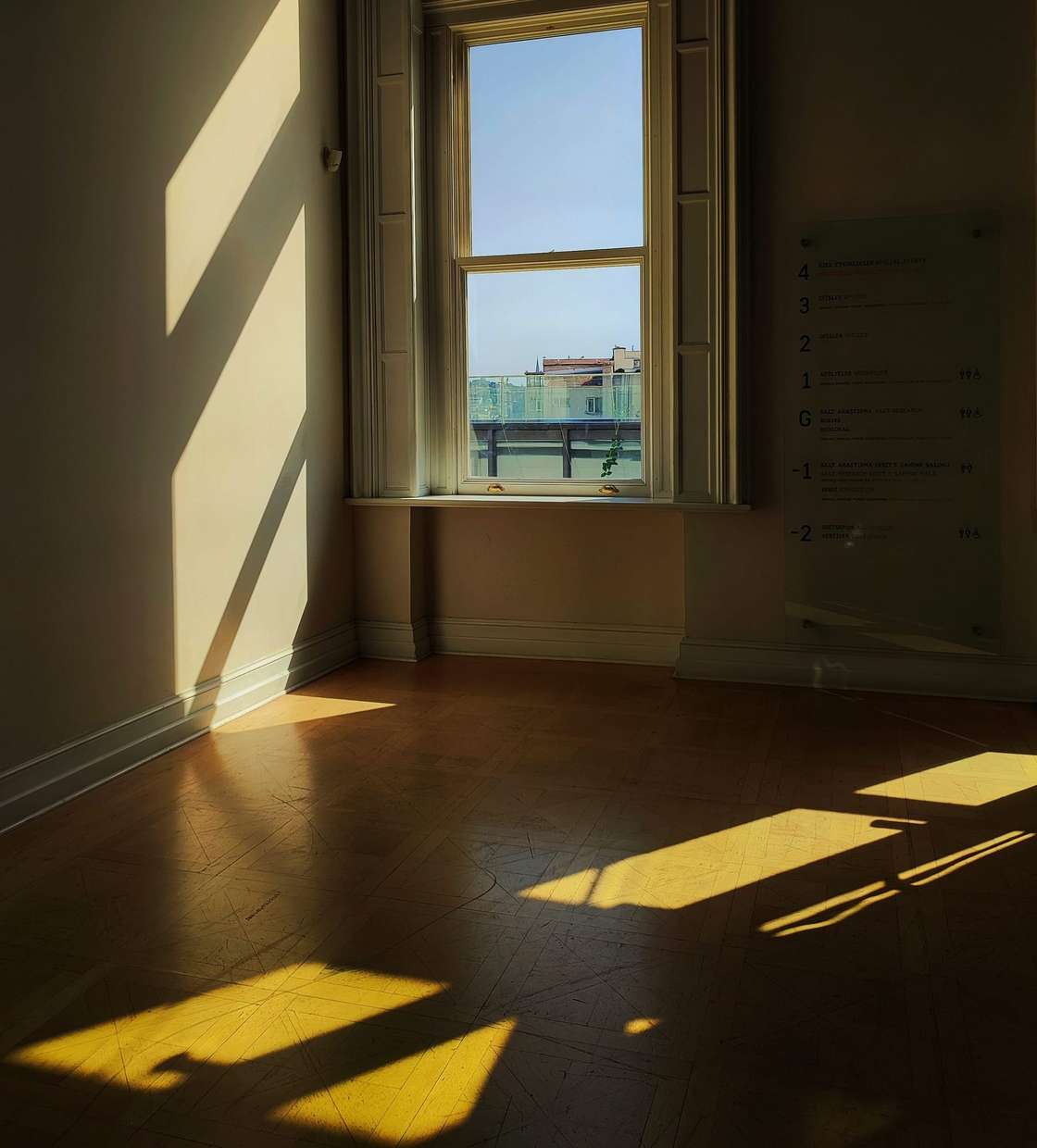 Habitación vacía con suelo de madera y una ventana por la que entra el sol de la tarde