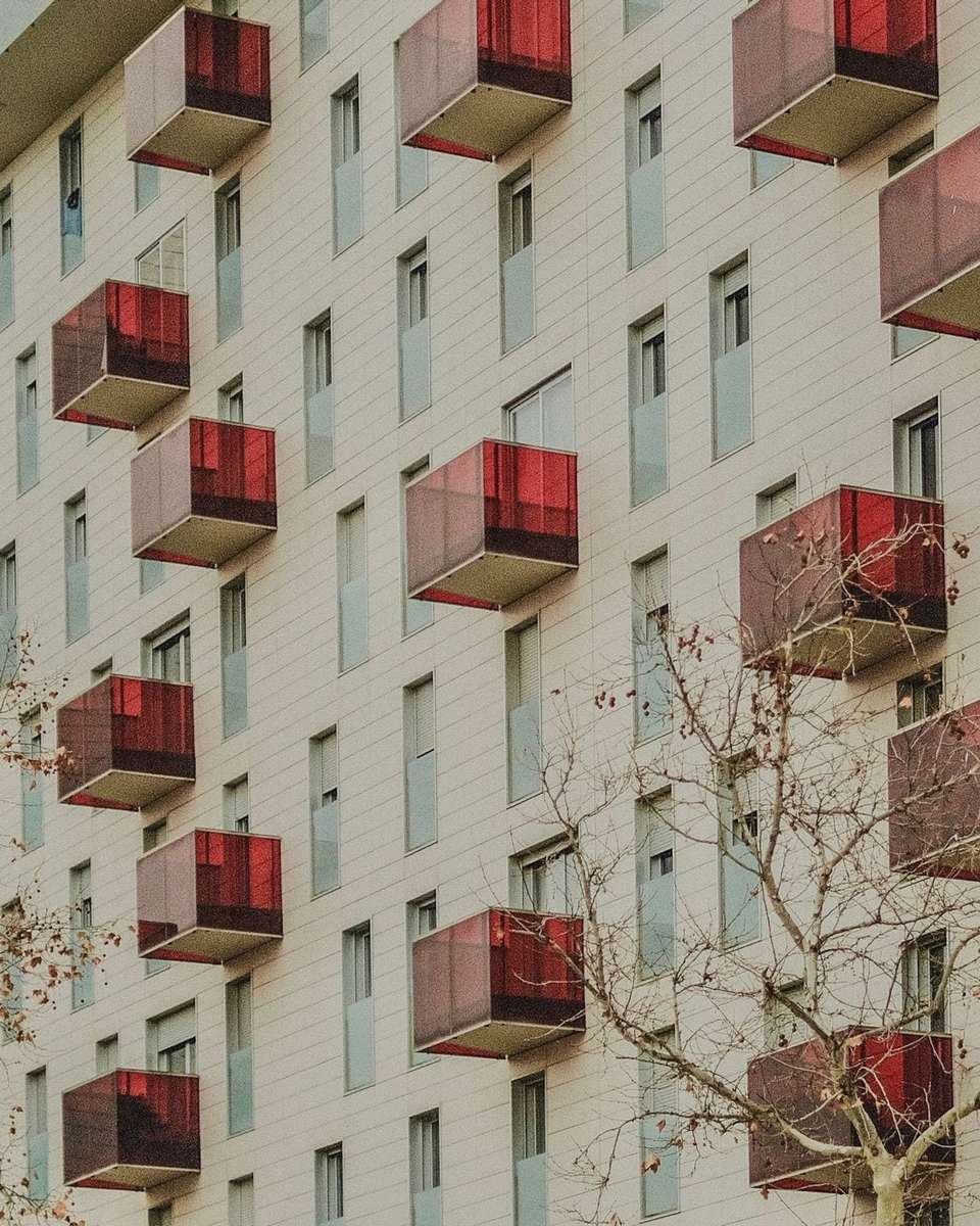 Fachada clara con balcones rojos y árboles delante en Zaragoza